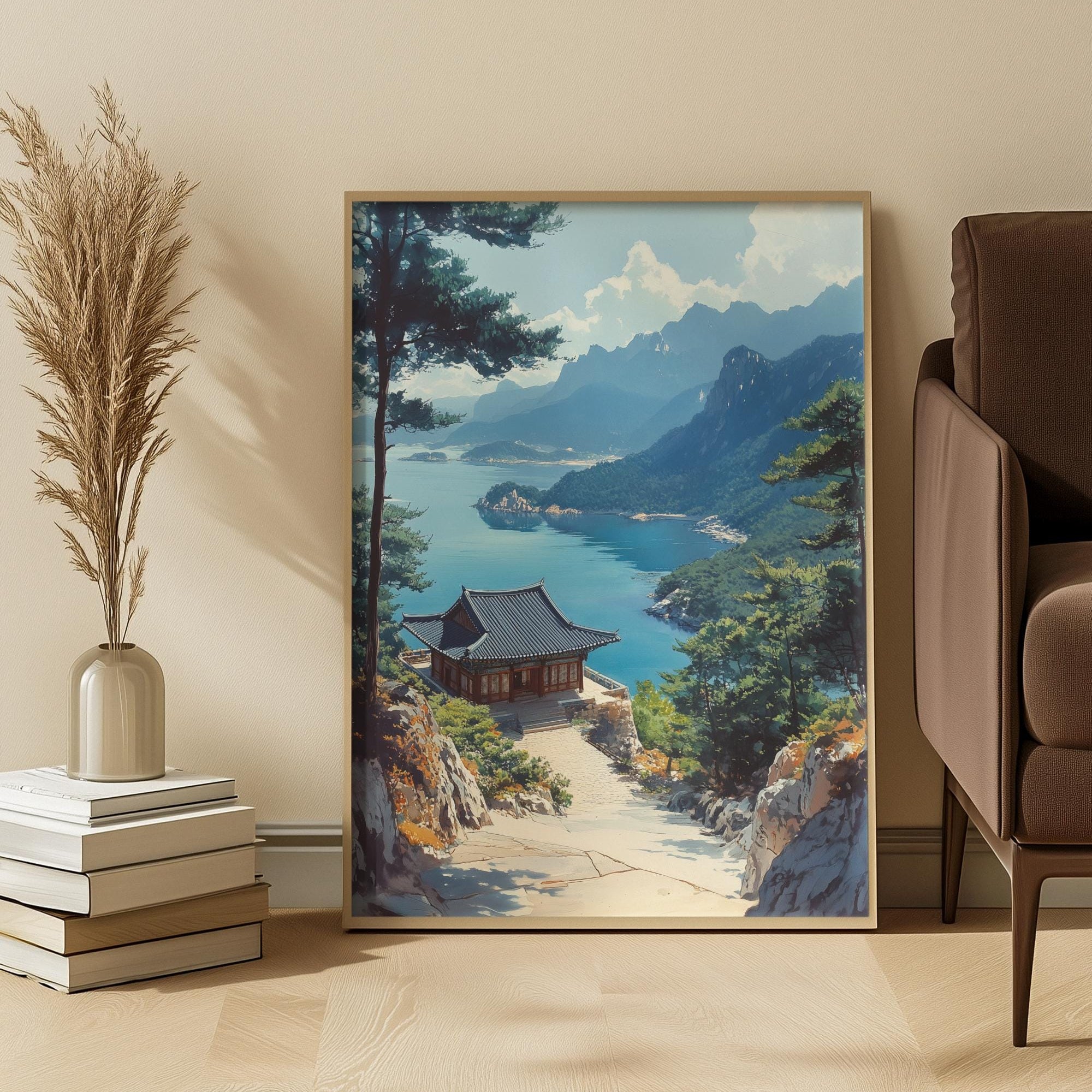 Framed landscape painting of a mountainous scene with a lake and traditional building, displayed in a room with a beige wall, books, and a vase.