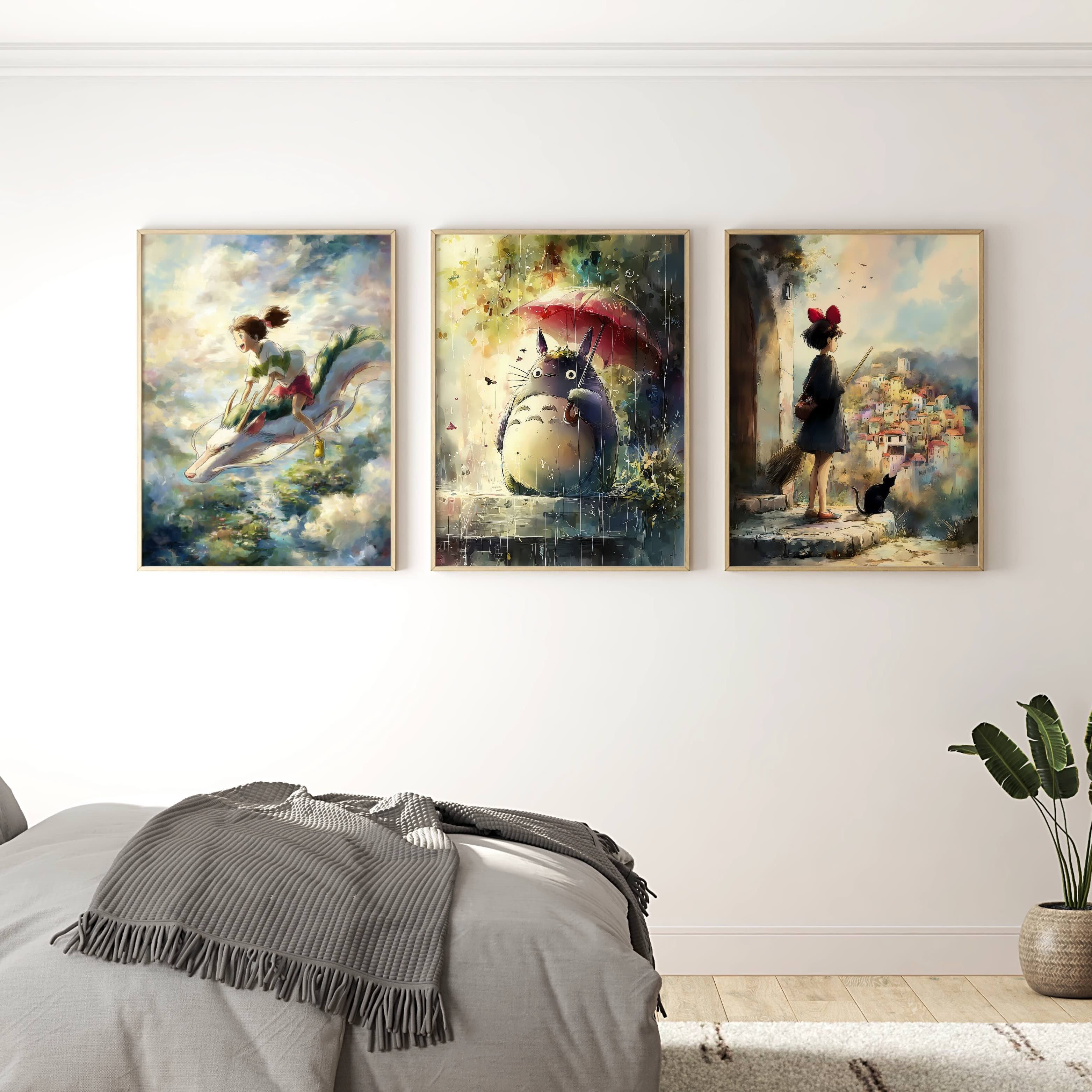 A three-piece framed canvas wall art set depicting Totoro from My Neighbor Totoro in a bedroom setting. The paintings are displayed on a white wall above a bed with gray bedding, with a wooden dresser and a potted plant in the background.