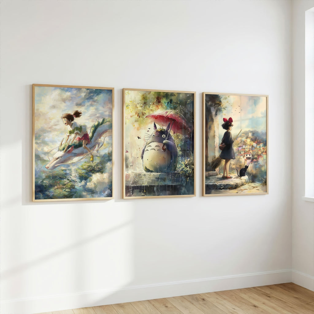 Three framed Spirited Away, My Neighbor Totoro, and Kiki’s Delivery Service in a fantasy paintings hang side by side on a white wall in a room with light wood flooring. The left painting shows a girl riding a dolphin, the center shows Totoro under a red umbrella, and the right shows a girl standing in a garden with a black cat.