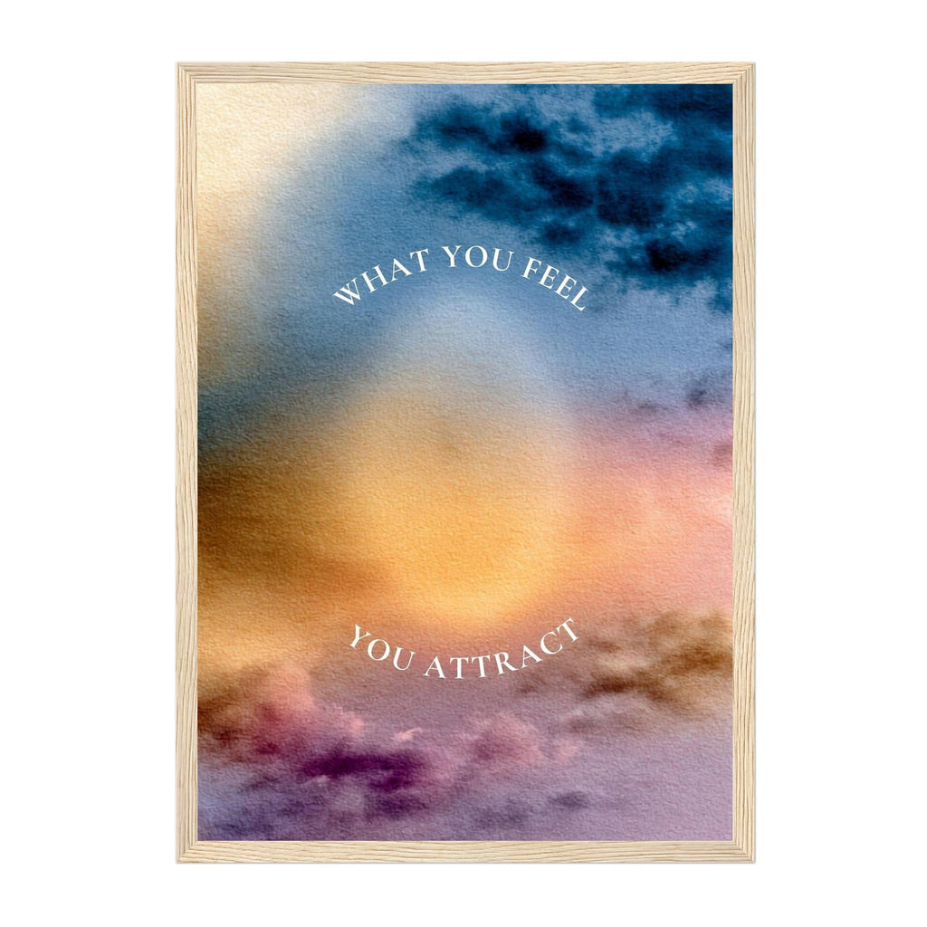A framed art print featuring a watercolor sunset sky with the text 'WHAT YOU FEEL YOU ATTRACT' in white arched lettering, set against a plain white background.