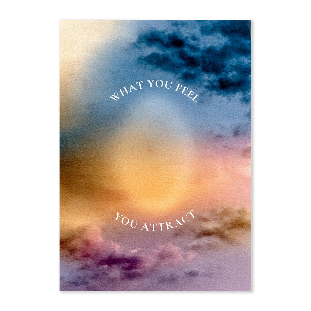 A vertical art print or card featuring an abstract watercolor sky design with the text 'WHAT YOU FEEL' arched at the top and 'YOU ATTRACT' curved at the bottom. The artwork shows blended blue, gold, peach, purple, and pink tones.