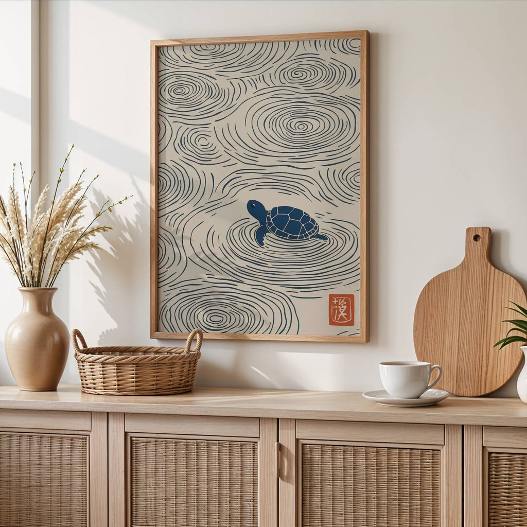 A framed wall art print featuring a blue turtle surrounded by swirling concentric lines on a cream background, styled in a warm, modern interior above a light wood cabinet with woven doors.
