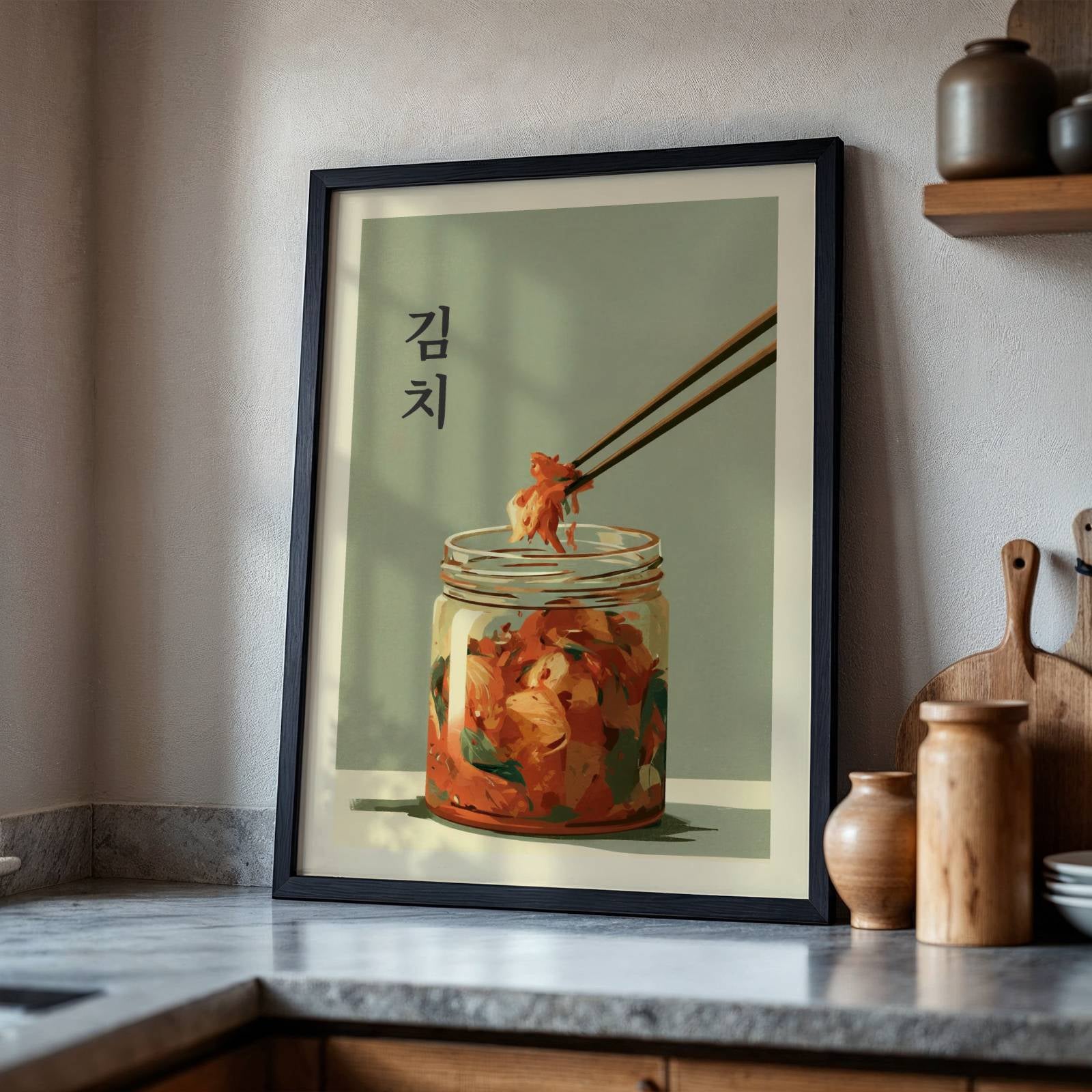A framed art print featuring Korean Kimchi in a glass jar with chopsticks lifting a piece, leaning against a kitchen wall on a marble countertop.