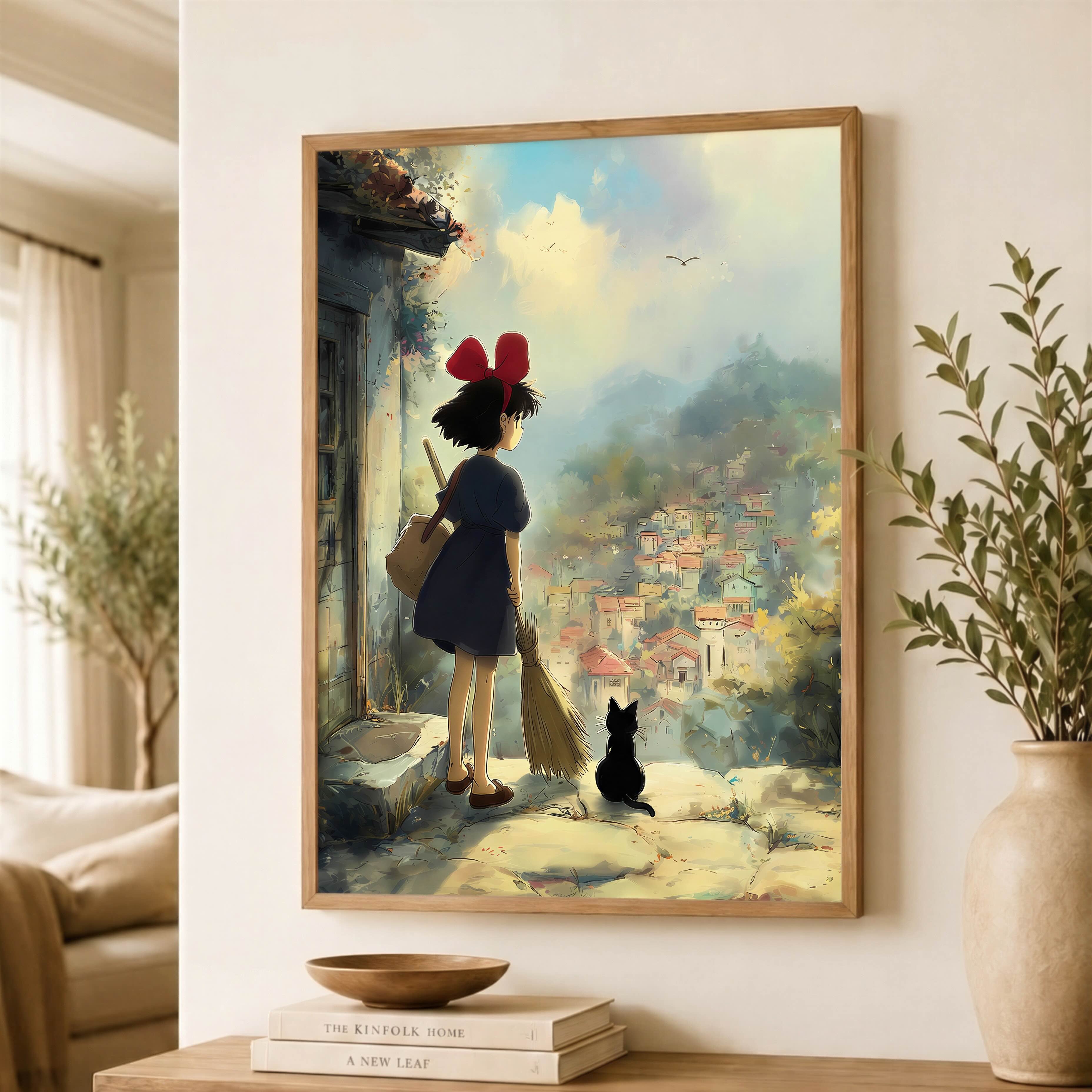 A framed art print of Kiki’s Delivery Service featuring Kiki and her black cat Jiji in a light wood frame, displayed on a wall above a wooden console table in a styled living room.